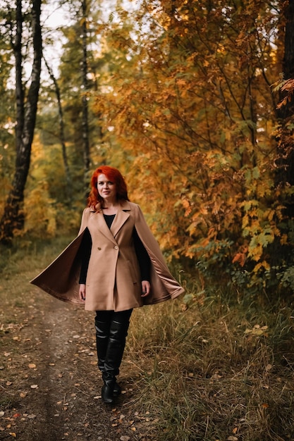 Giovane bella donna con testa rossa in cappotto beige che cammina nella foresta di autunno