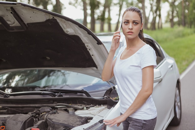 Giovane bella donna con un'automobile rotta sulla strada