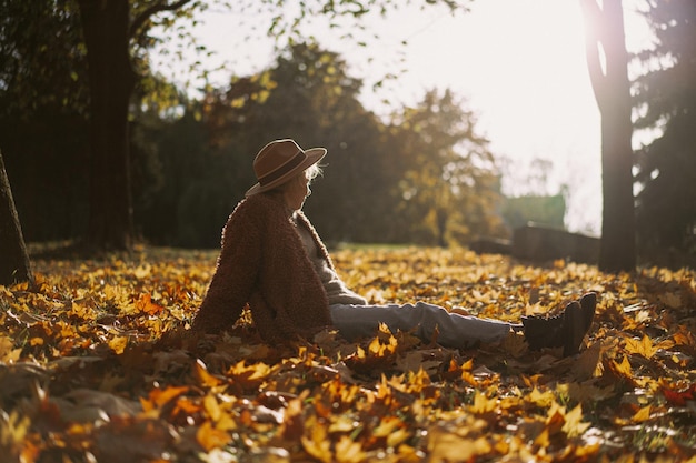 Giovane bella donna con un cappello in un parco autunnale, una borsa di corda con arance, una donna vomita foglie d'autunno. Umore autunnale, colori vivaci della natura.