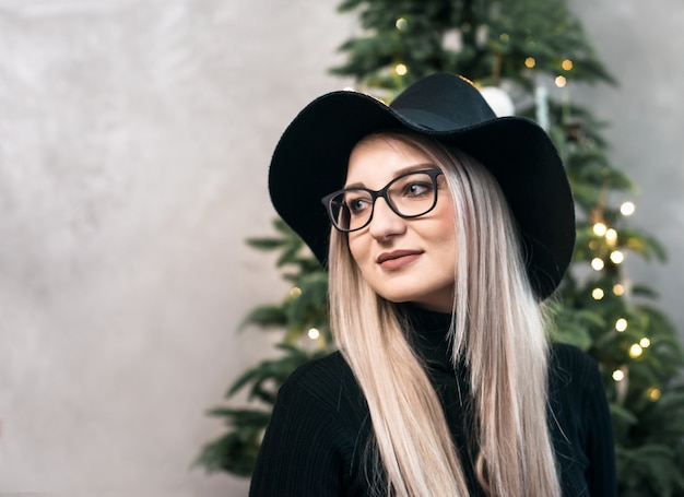 Giovane bella donna con un cappello nero sopra l'albero di Natale.