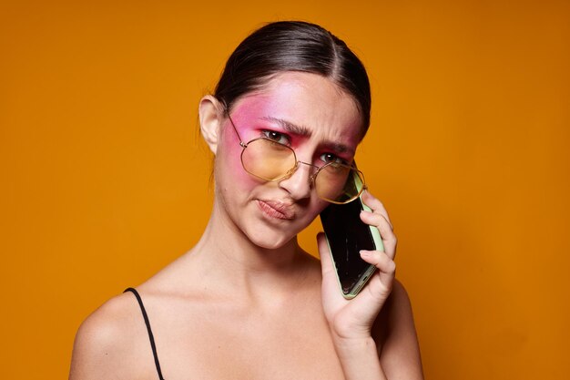 Giovane bella donna con un telefono in mano trucco luminoso in posa emozioni moda sfondo giallo inalterato