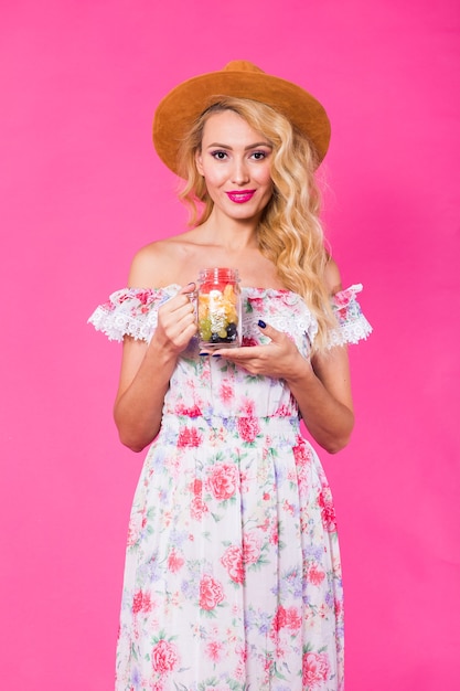 Giovane bella donna con vaso di frutta sulla parete rosa