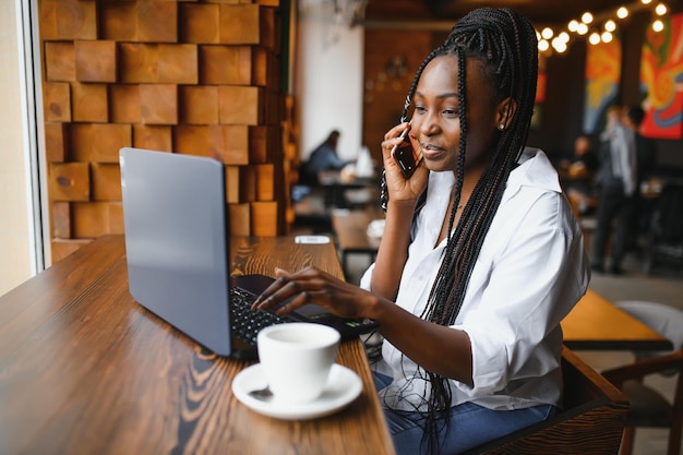 Giovane bella donna d'affari afroamericana che parla al telefono mentre lavora in un caffè