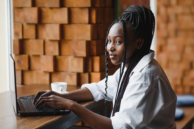Giovane bella donna d'affari afroamericana utilizzando laptop mentre si lavora nella caffetteria