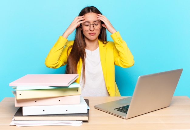 Giovane bella donna d'affari che sembra concentrata, premurosa e ispirata, che fa brainstorming e immagina con le mani sulla fronte