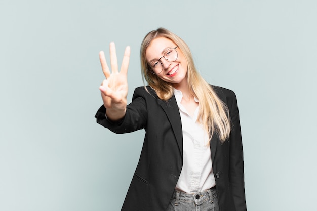 Giovane bella donna d'affari sorridente e dall'aspetto amichevole, mostrando il numero tre o il terzo con la mano in avanti, conto alla rovescia