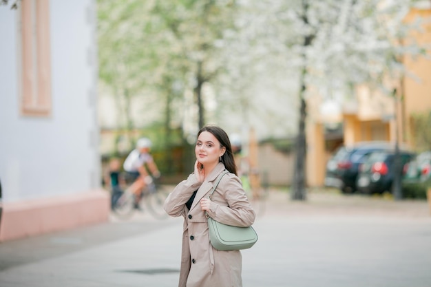 Giovane bella donna di 19 anni in abiti eleganti Modello con capelli scuri in abiti casual cammina attraverso la città fiorita primaverile Caldo