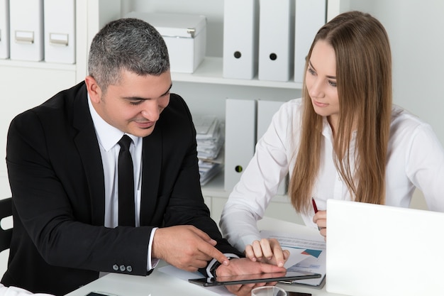 Giovane bella donna di affari che si consulta con il suo collega maschio che mostra qualcosa sul tablet PC. Partner che discutono documenti e idee