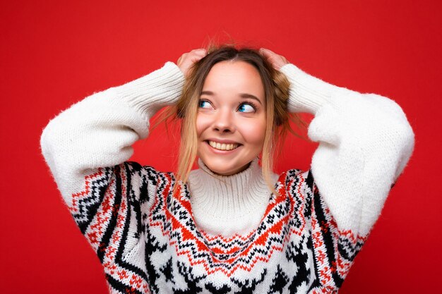 Giovane bella donna. Donna alla moda in maglione invernale casual. La femmina positiva mostra le emozioni facciali. Modello divertente isolato su sfondo rosso.