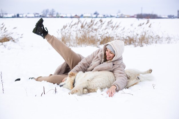 Giovane bella donna e il suo cane golden retriever che si divertono in inverno