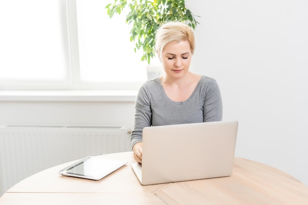 Giovane bella donna felice che per mezzo del computer portatile, all'interno.