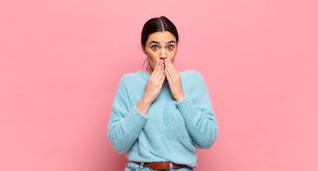 giovane bella donna felice ed eccitata, sorpresa e stupita che copre la bocca con le mani, ridacchiando con un'espressione carina