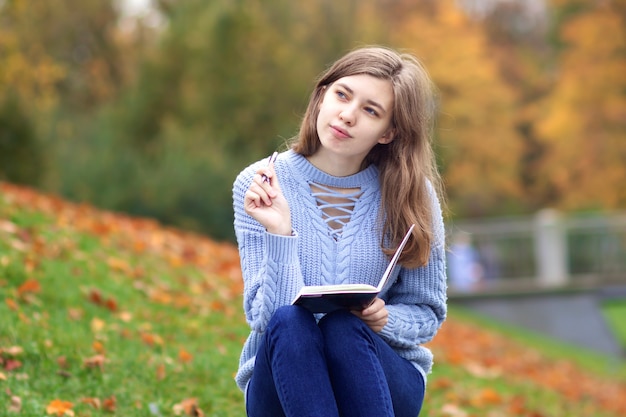 Giovane bella donna felice, studente adolescente sta studiando all'aperto nel parco scrivendo in taccuino o