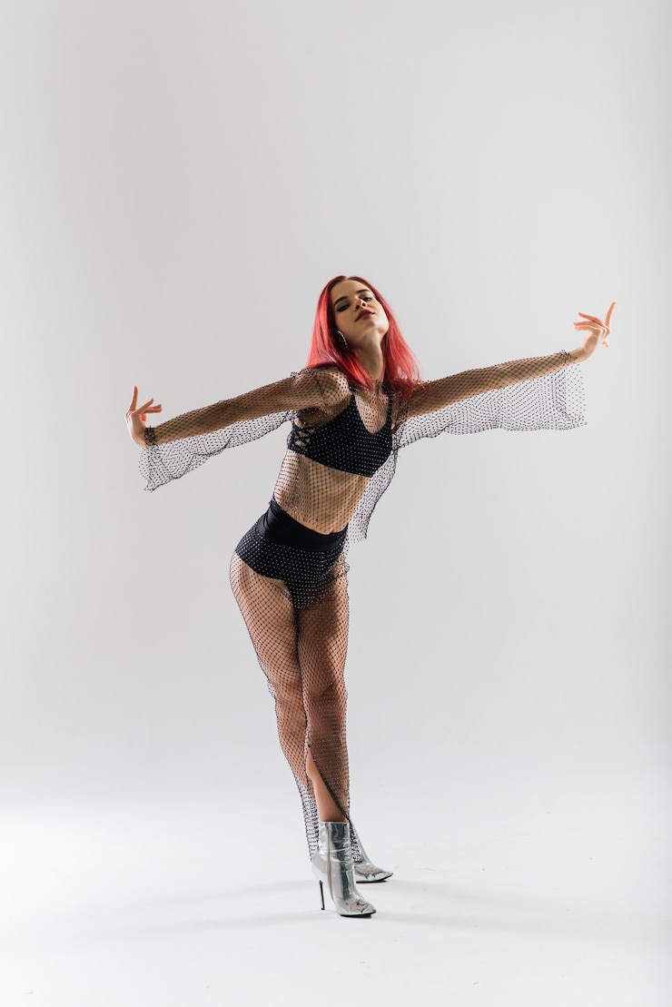 Foto giovane bella donna flessibile in una tuta nera e tacchi alti è in posa in uno studio di danza.