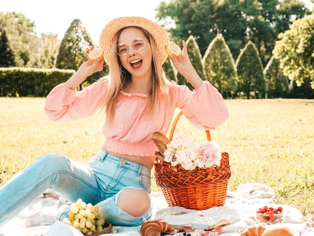 Giovane bella donna hipster in jeans estivi alla moda, maglietta rosa e cappello. Donna che fa picnic all'esterno.