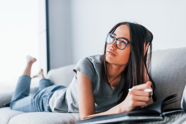 Giovane bella donna in abiti casual sdraiato a casa da solo con blocco note e penna.