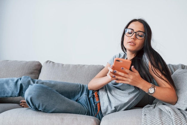 Giovane bella donna in abiti casual sdraiato a casa da solo con lo smartphone in mano.