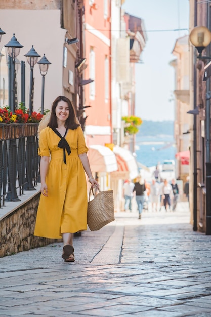 Giovane bella donna in abito giallo che cammina per il mare di piccole strade della città di Porec sullo sfondo