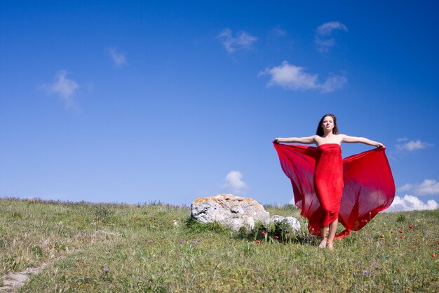 Giovane bella donna in abito rosso in piedi sul campo