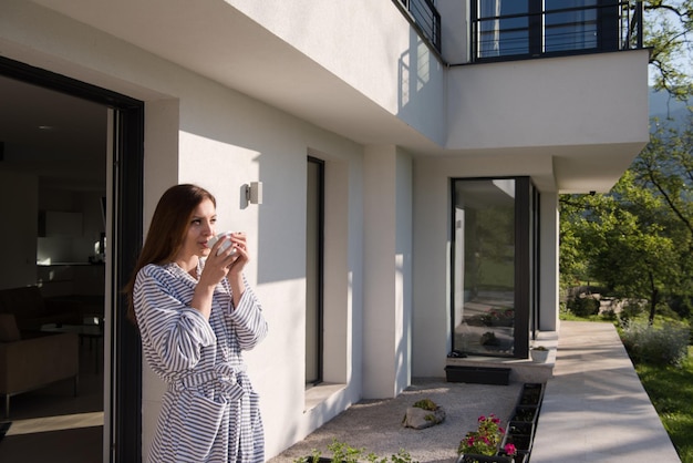 giovane bella donna in accappatoio godendo il caffè del mattino davanti alla sua villa di lusso