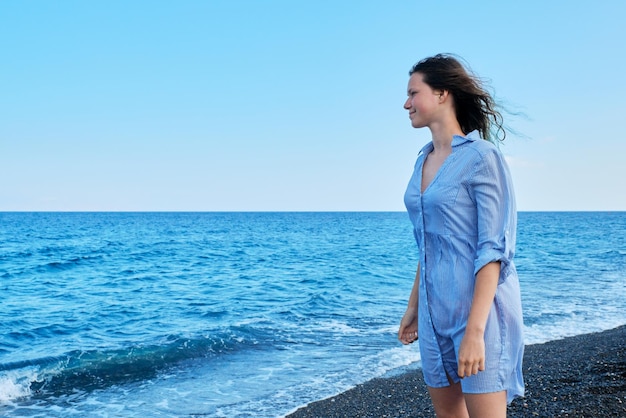 Giovane bella donna in camicia blu con i capelli bagnati sulla spiaggia guardando il cielo del mare