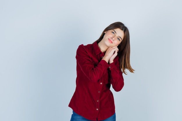 Giovane bella donna in camicia in posa mentre tiene la mano vicino al viso e sembra allegra