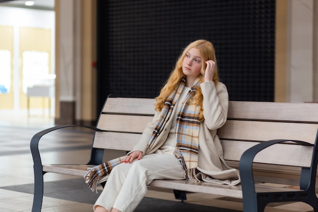 Giovane bella donna in cappotto leggero che si siede sulla panchina all'interno di un centro commerciale shoping