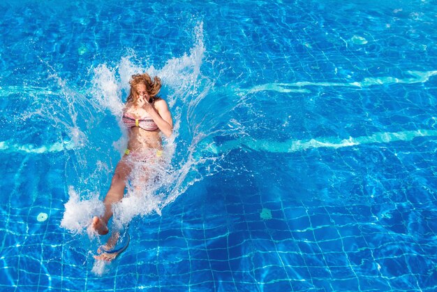 Giovane bella donna in costume da bagno che salta in piscina con una spruzzata