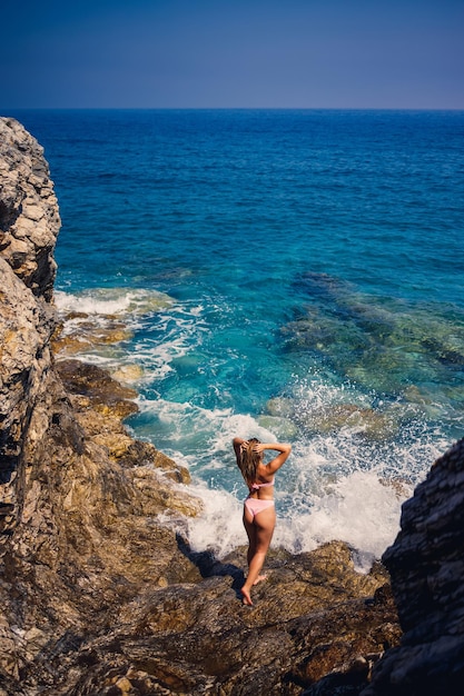 Giovane bella donna in costume da bagno si trova su una spiaggia rocciosa del Mar Mediterraneo Il concetto di ricreazione in mare Messa a fuoco selettiva