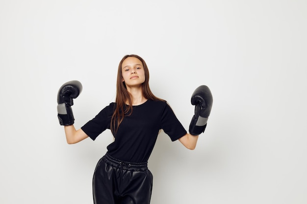 Giovane bella donna in guanti da boxe uniformi sportivi neri in posa sullo sfondo isolato