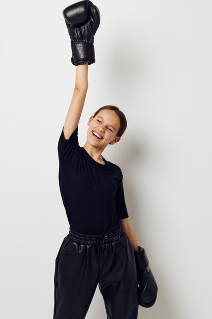 Giovane bella donna in guanti da boxe uniformi sportivi neri in posa sullo sfondo isolato