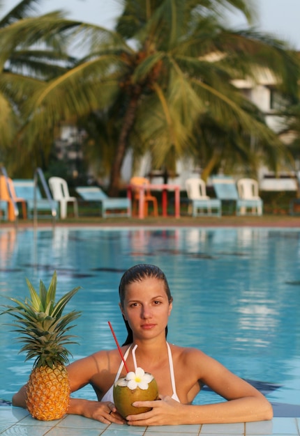 Giovane bella donna in piscina con cocco e ananas