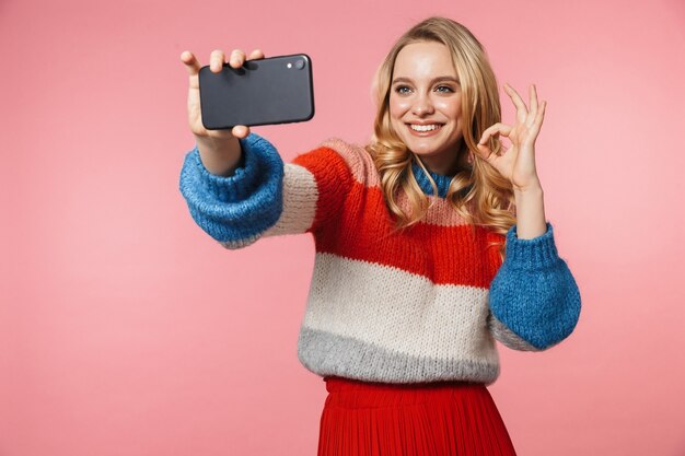 giovane bella donna in posa isolata sul muro rosa scatta un selfie con il cellulare