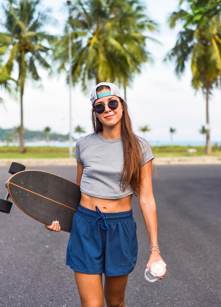 Giovane bella donna in un berretto in piedi e in possesso di skateboard con una faccia fredda