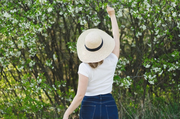 Giovane bella donna in un cappello tra alberi in fiore vista posteriore