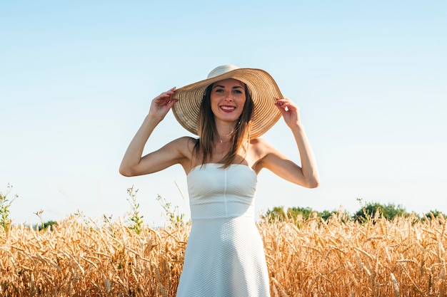 Giovane bella donna in un vestito bianco e un cappello sul campo di un suocera.