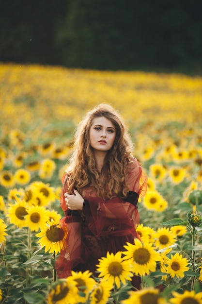 Giovane bella donna in un vestito tra i girasoli fioriti. Agro-cultura.