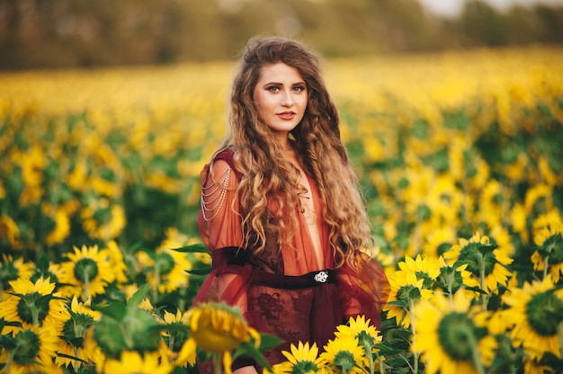 Giovane bella donna in un vestito tra i girasoli fioriti. Agro-cultura.