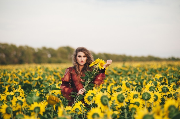 Giovane bella donna in un vestito tra i girasoli fioriti. Agro-cultura.