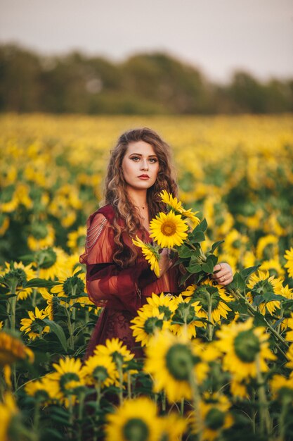 Giovane bella donna in un vestito tra i girasoli fioriti. Agro-cultura.