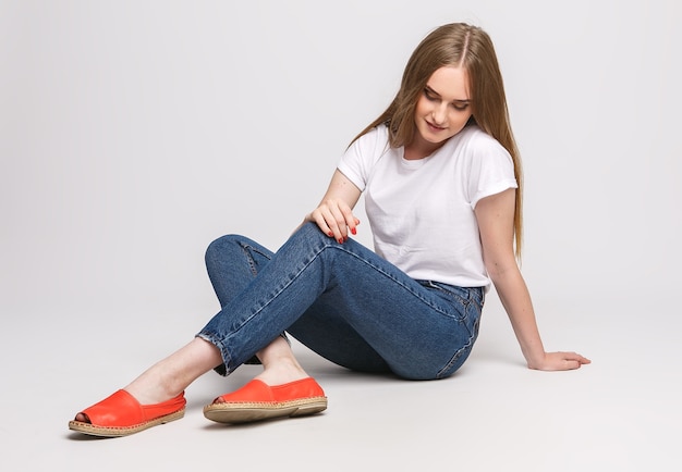 Giovane bella donna in una maglietta bianca e jeans su uno sfondo bianco