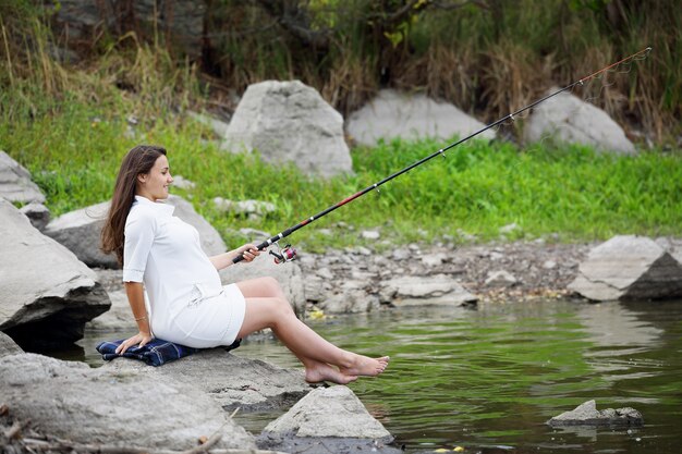 Giovane bella donna incinta che pesca sulla sponda del fiume