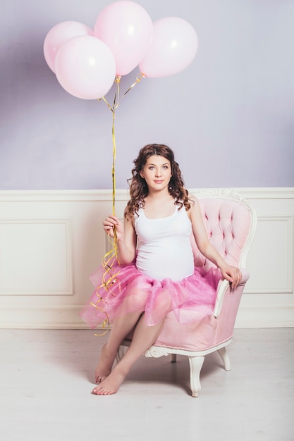 Giovane bella donna incinta con palloncini rosa e una gonna da balletto rosa su sfondo retrò