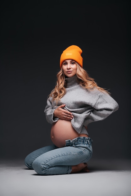 Giovane bella donna incinta seduta sul muro nero