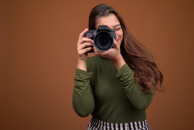 Giovane bella donna indiana con fotocamera contro il muro marrone