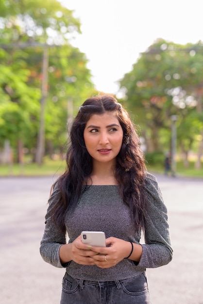 Giovane bella donna indiana pensando durante l'utilizzo del telefono nelle strade del parco