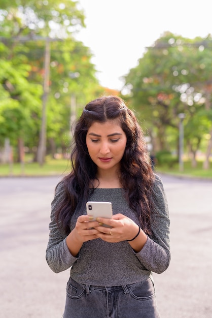 Giovane bella donna indiana utilizzando il telefono nelle strade del parco