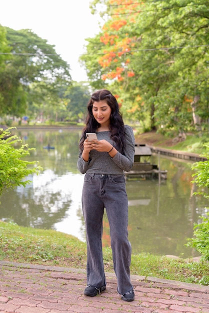 Giovane bella donna indiana utilizzando il telefono presso il parco all'aperto