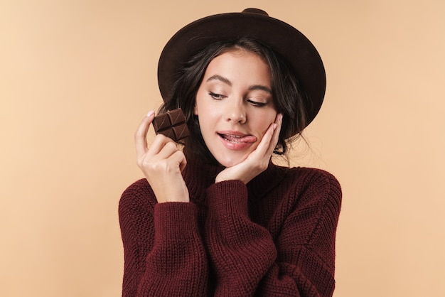 giovane bella donna isolata sopra la parete beige della parete che tiene le labbra leccate di cioccolato.