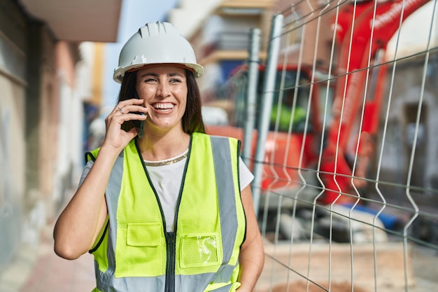 Giovane bella donna ispanica architetto sorridente parlando fiducioso sullo smartphone in strada